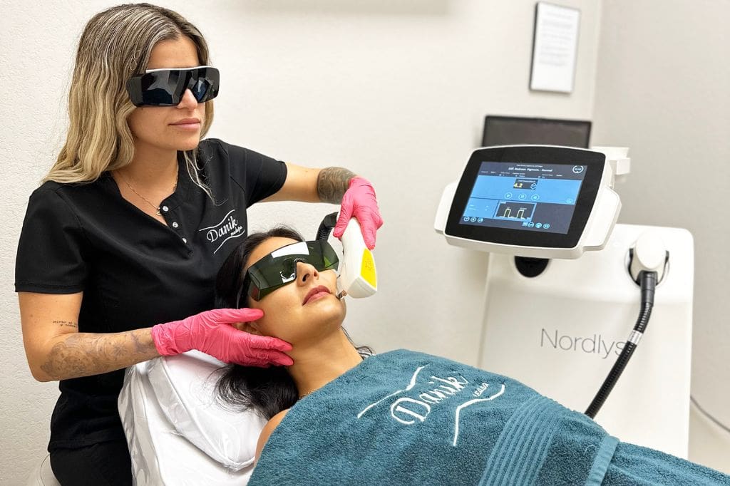 Specialist Wearing Black Uniform And Protective Glasses Applies IPL Facial Rejuvenation Treatment To A Woman In A Blue Towel And Protective Glasses