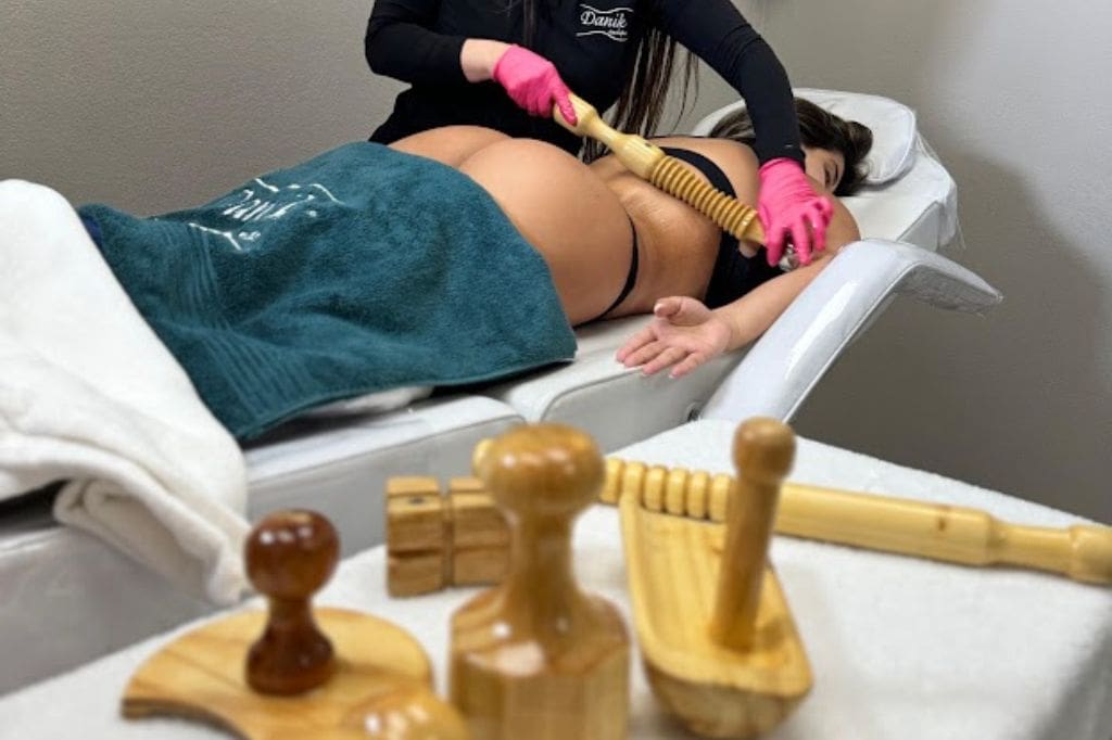 Woman Receiving Wood Therapy Body Sculpting Treatment On Her Back From A Specialist In Black Uniform And Pink Gloves