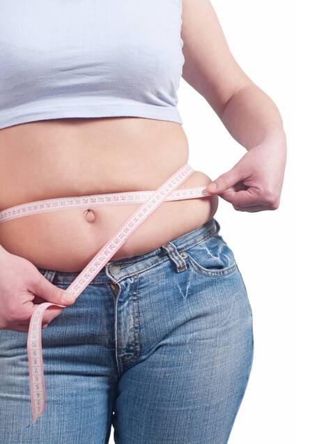 Close-up of a person measuring their waistline with a tape measure, representing weight loss results from Fat 30X.